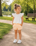 Meisje draagt een witte Dirkje top met rufflemouwen en een perzikkleurige Dirkje short uit de zomercollectie.